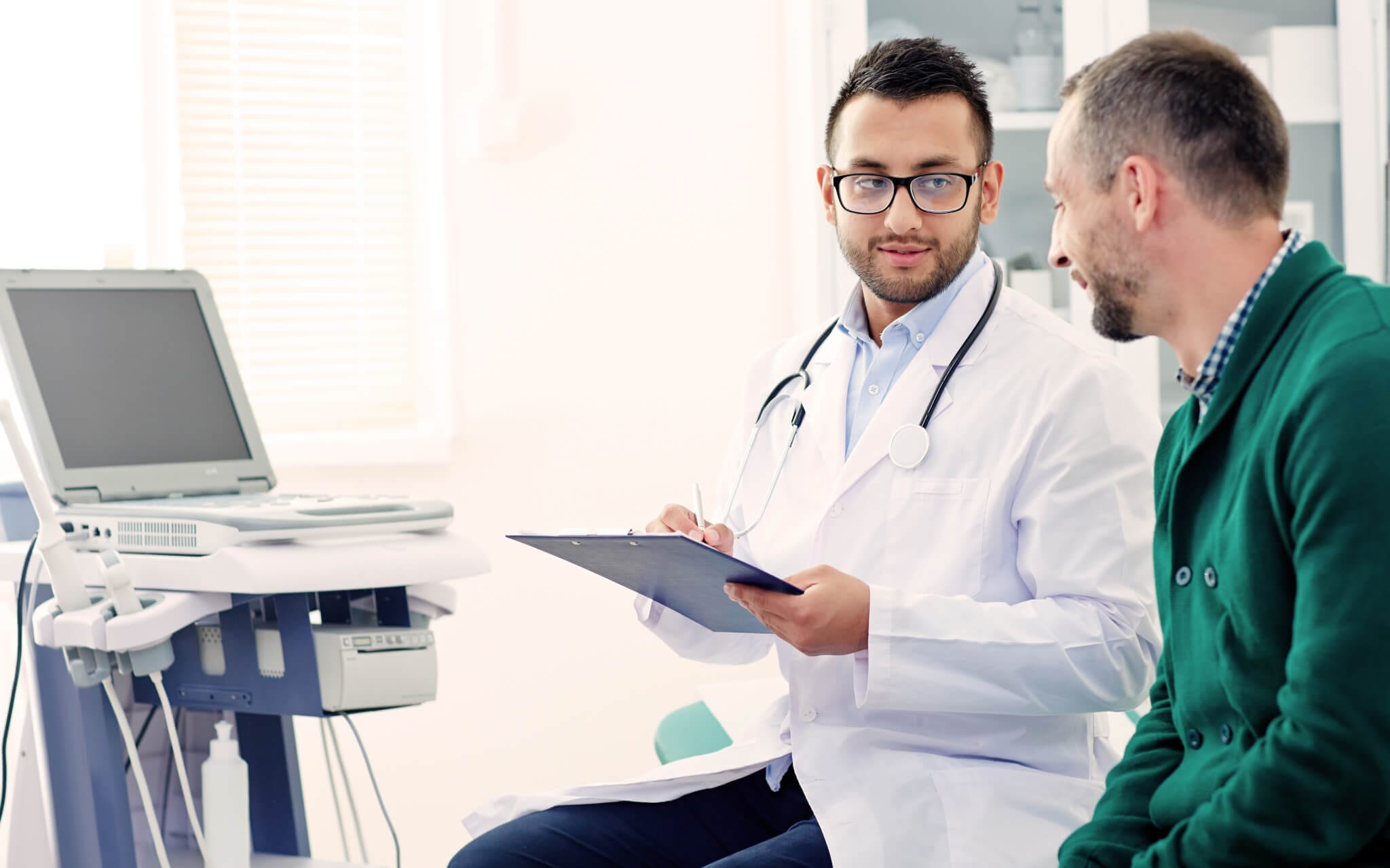 A doctor goes over his patient's mesothelioma medical records and timeline on his clipboard as his patient looks on.