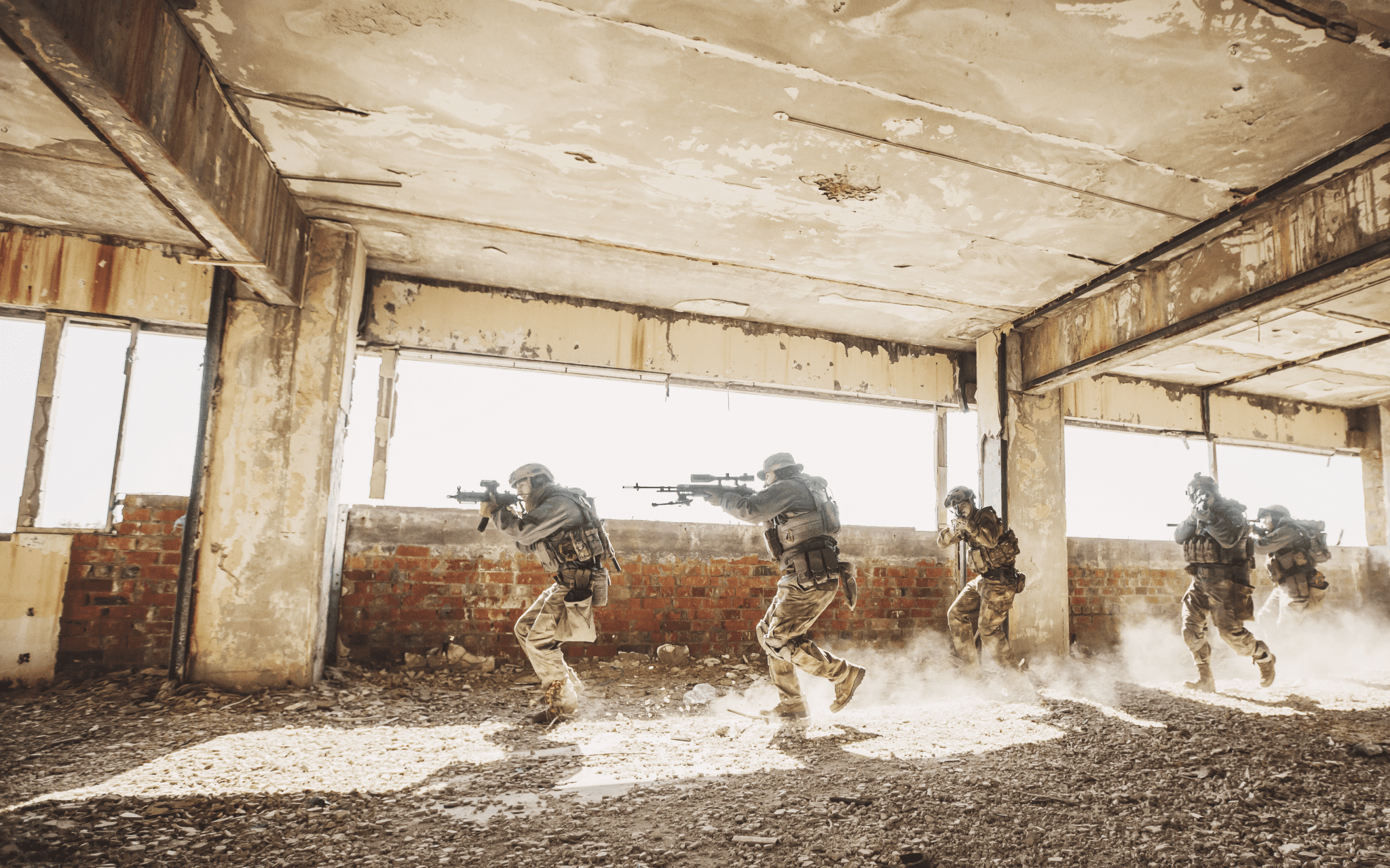 Army veterans with guns drawn jogging through a war torn building.