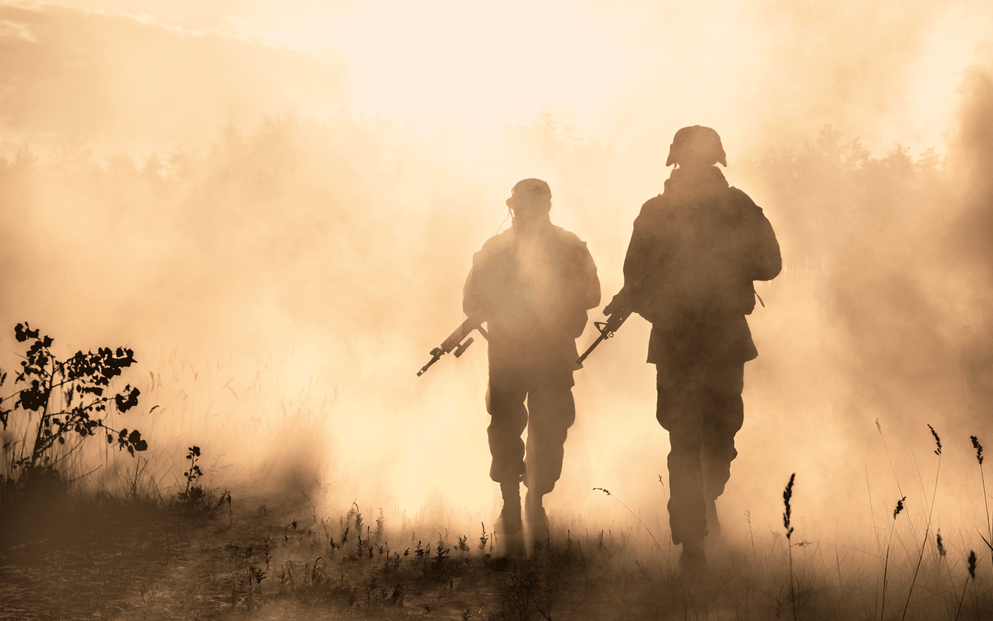 The silhouettes of a marine walking alongside another marine with weapons.