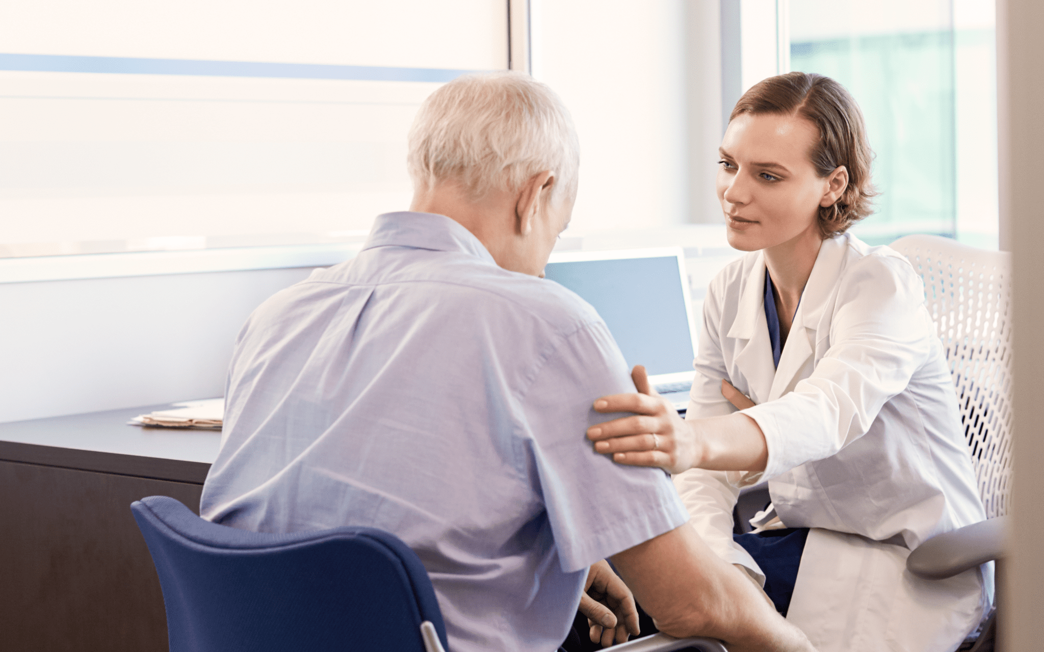 Elderly man is comforted by female mesothelioma doctor at her medical office.