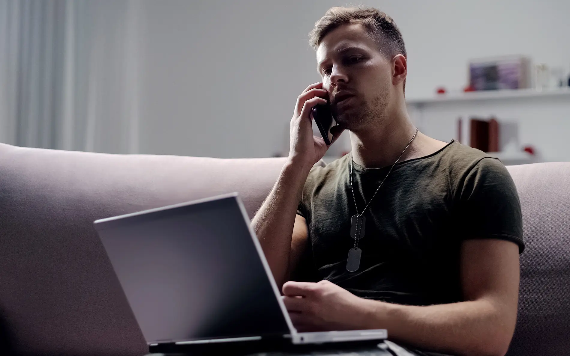 A veteran with dogtags on his laptop calling someone on his cell phone.