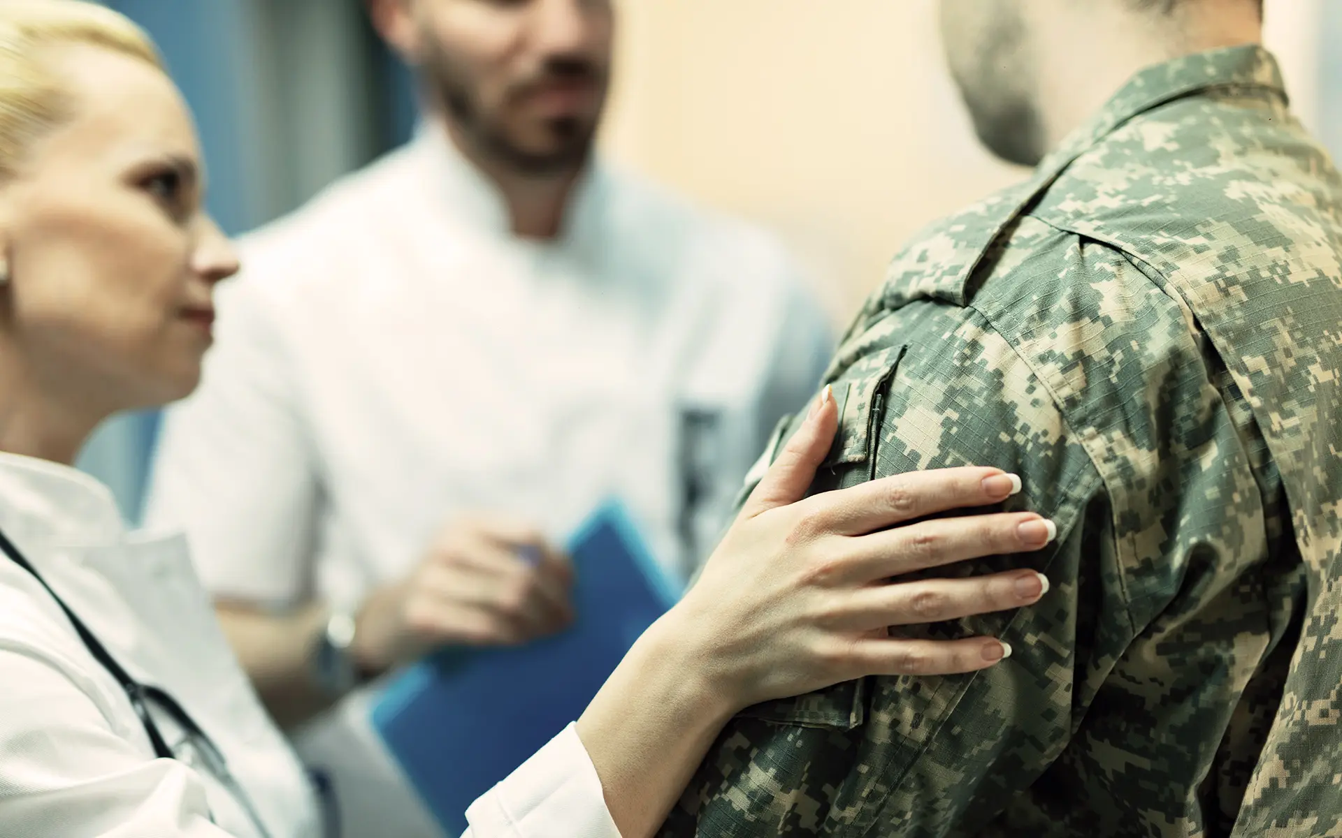 A female doctors pats the shoulder of a veteran while another doctor looks on.