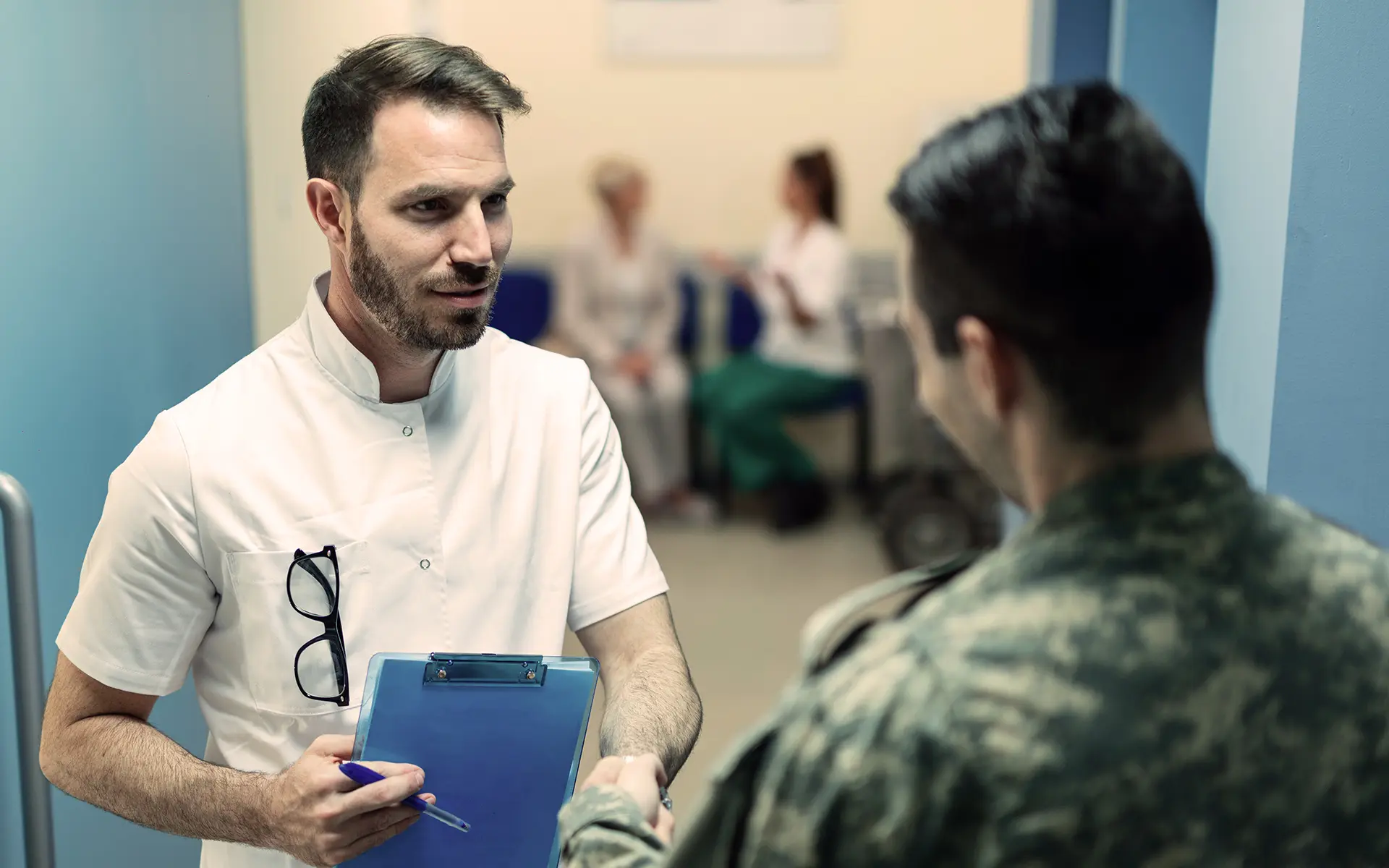 A doctor shaking the hand of a veteran as another patient and doctor sit in the background.