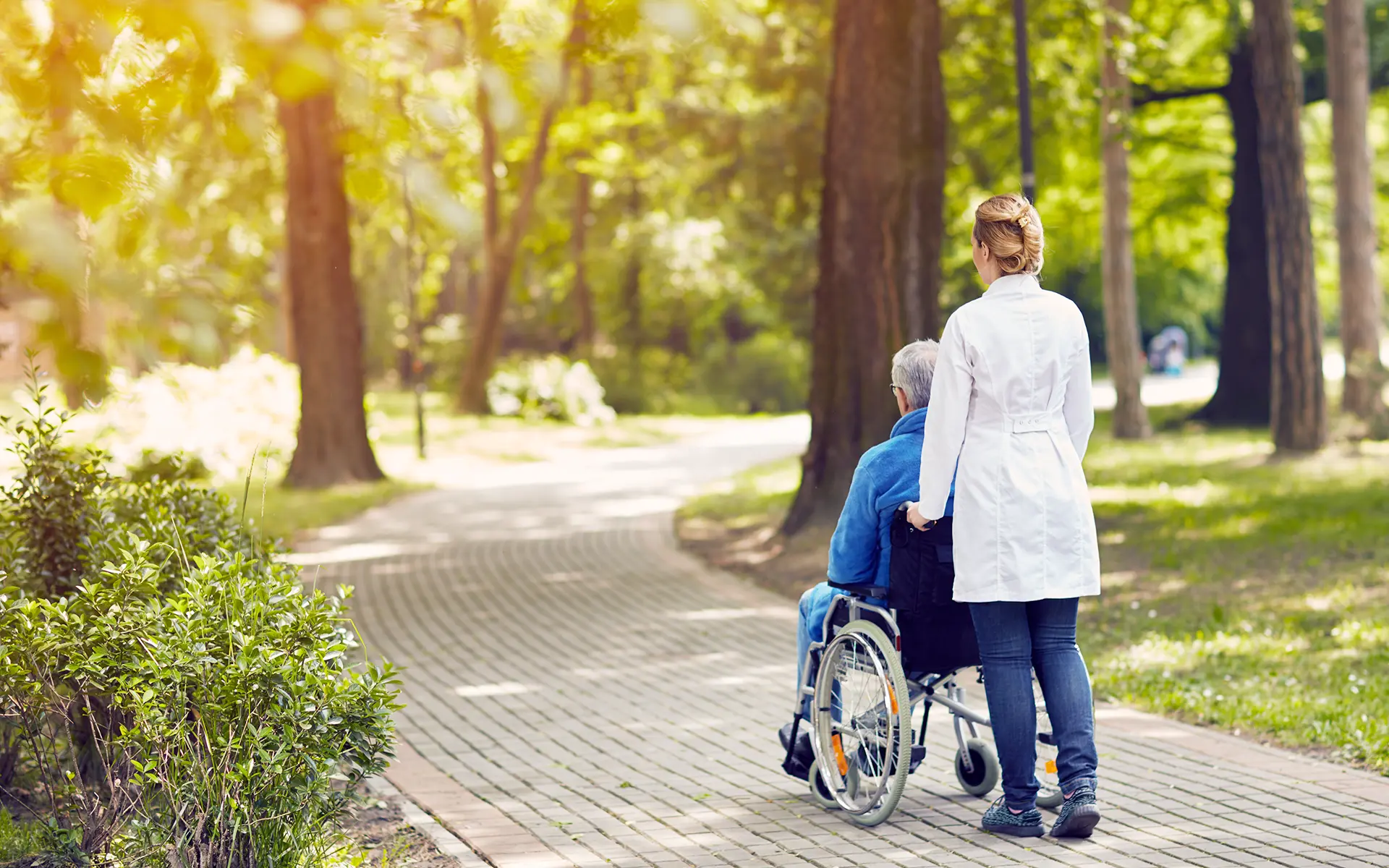 A hospice nurse taking an elderly man on a walk in his wheelchair.