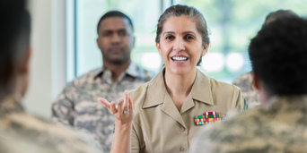 A female military officer instructs two veterans who face her as another soldier watches on behind her