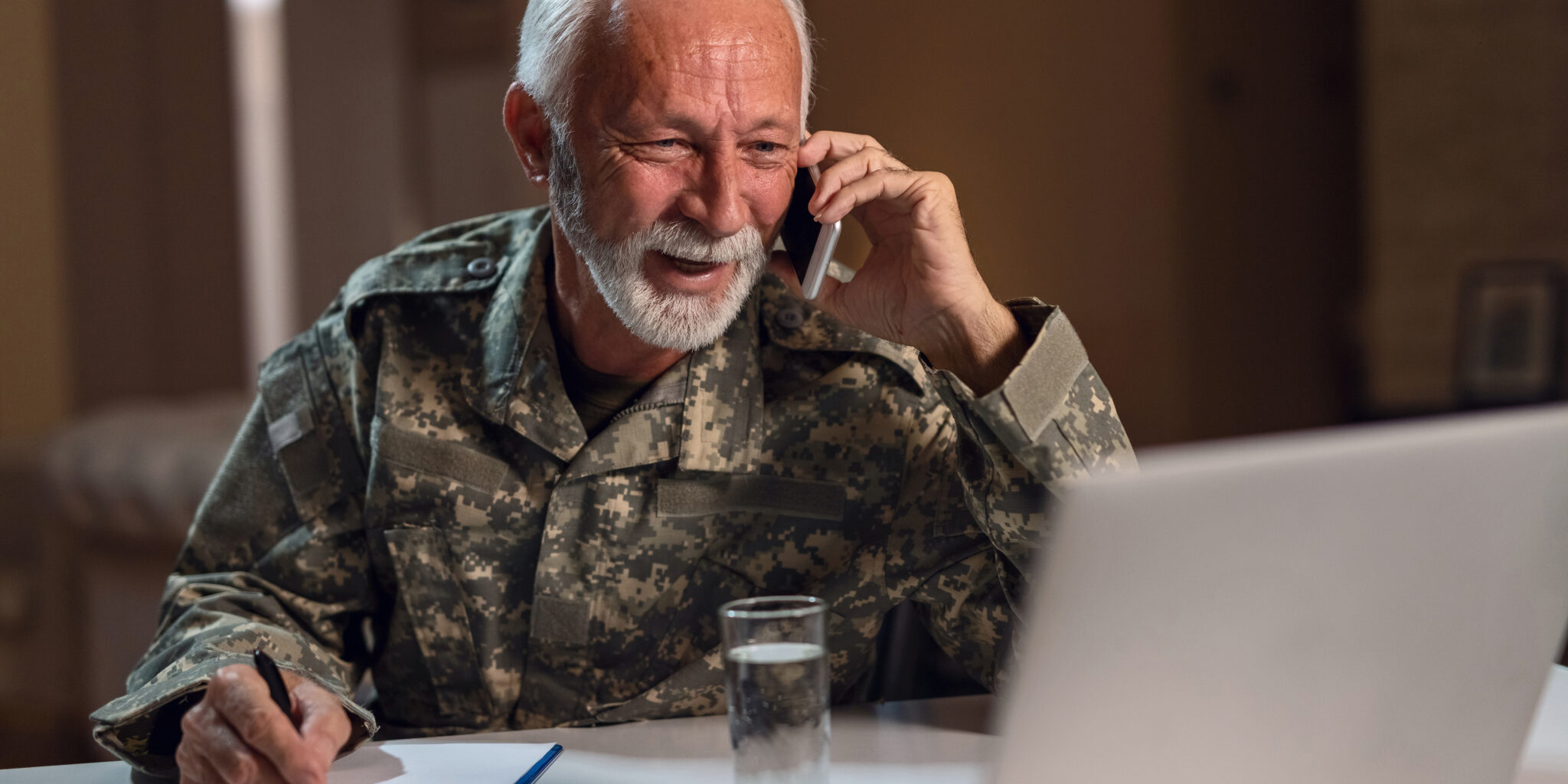 Happy senior male veteran talking on the phone and looking at the computer