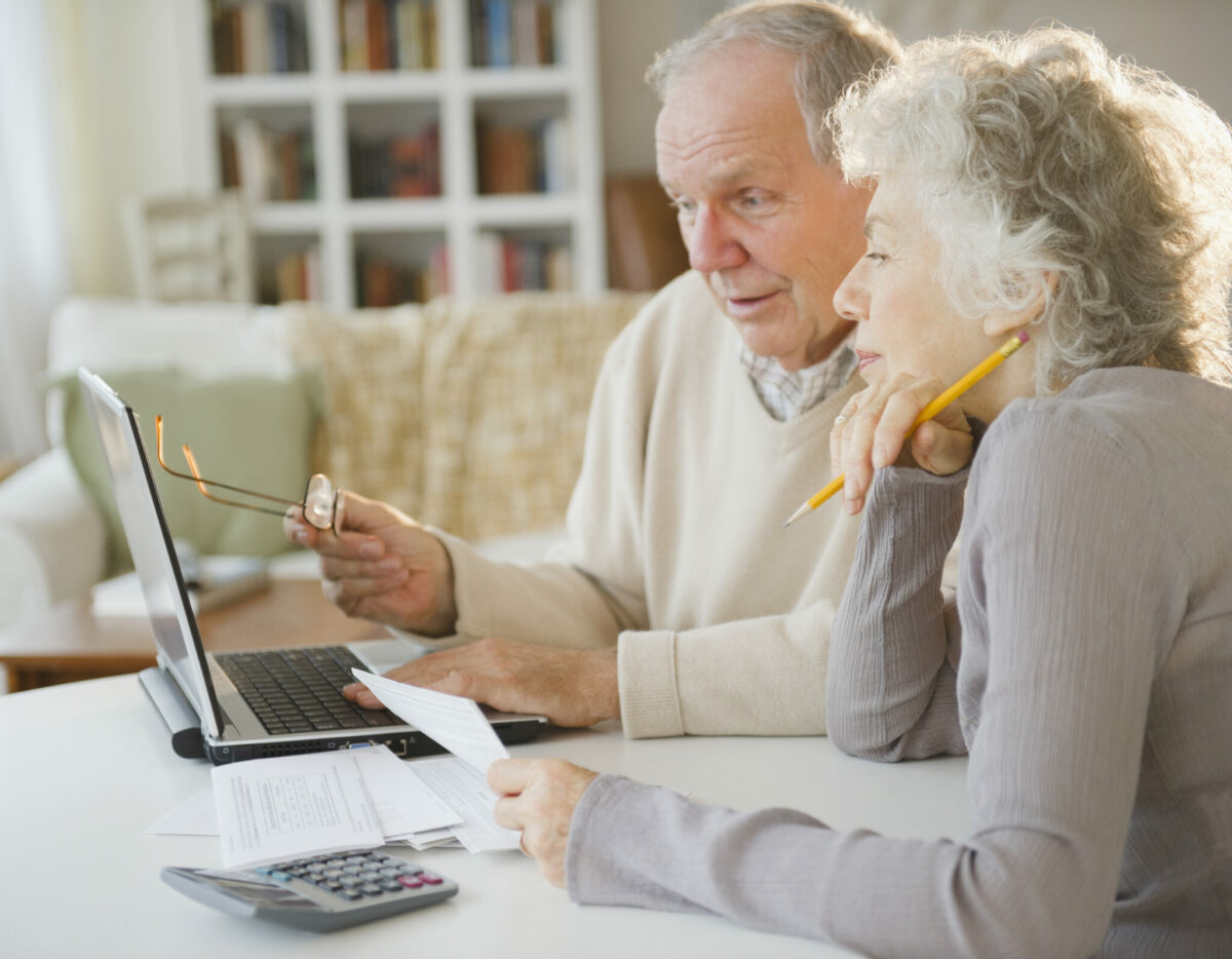 Elderly couple works on together on paperwork with a laptop in front of them