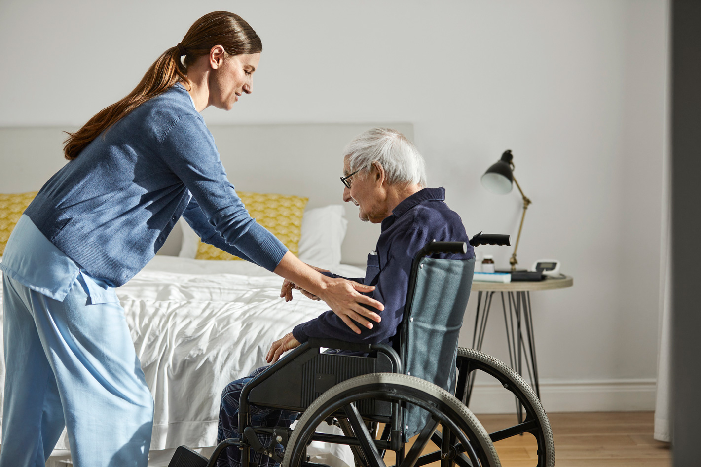 Young caregiver helping senior man in wheel chair.