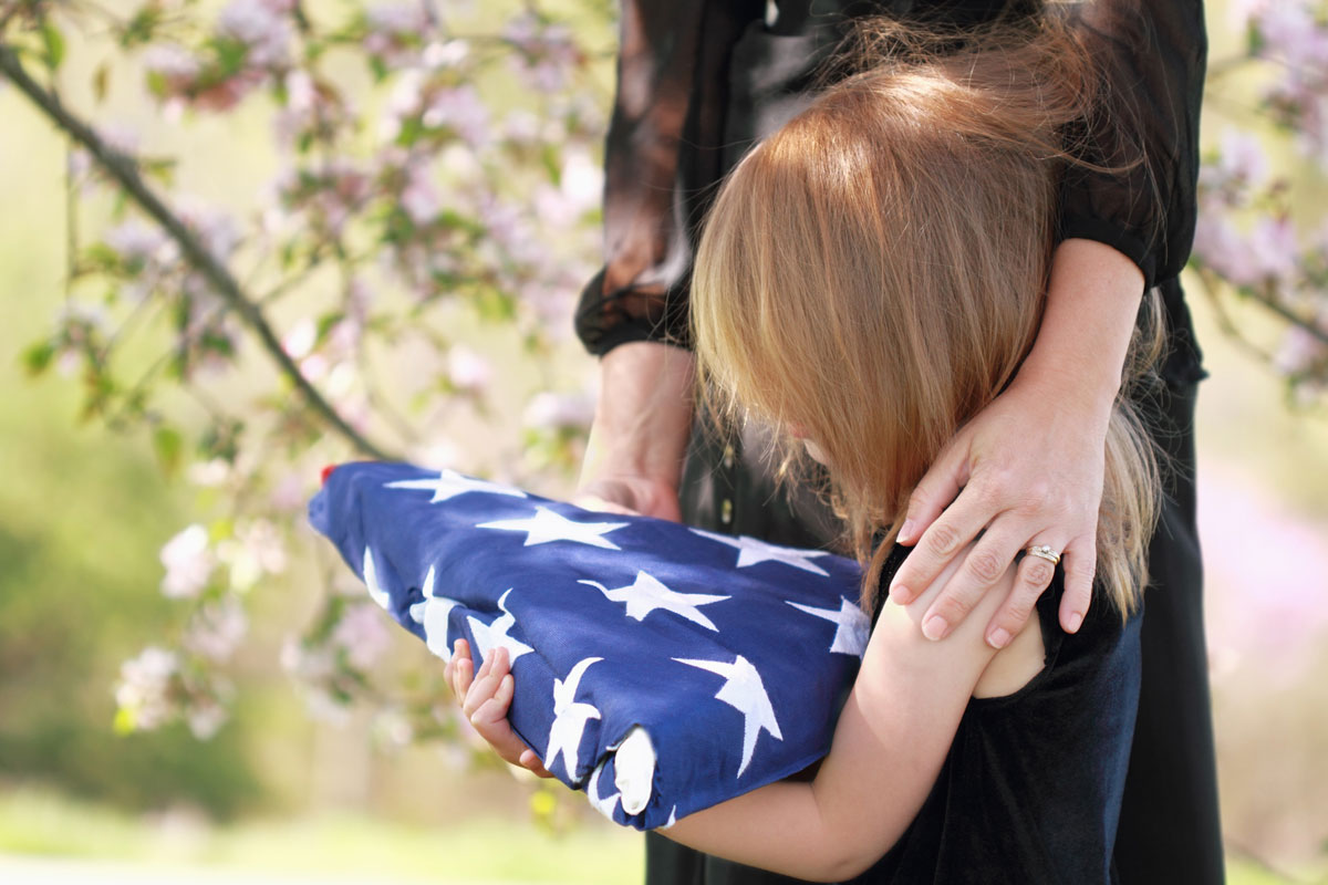 grieving young girl with mother holding folded flag at veteran funeral