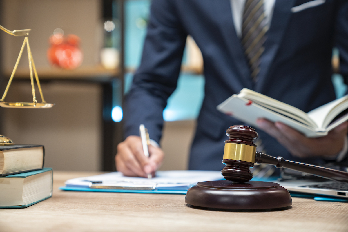 closeup of a lawyer in their office writing on paperwork with a gavel in front of them