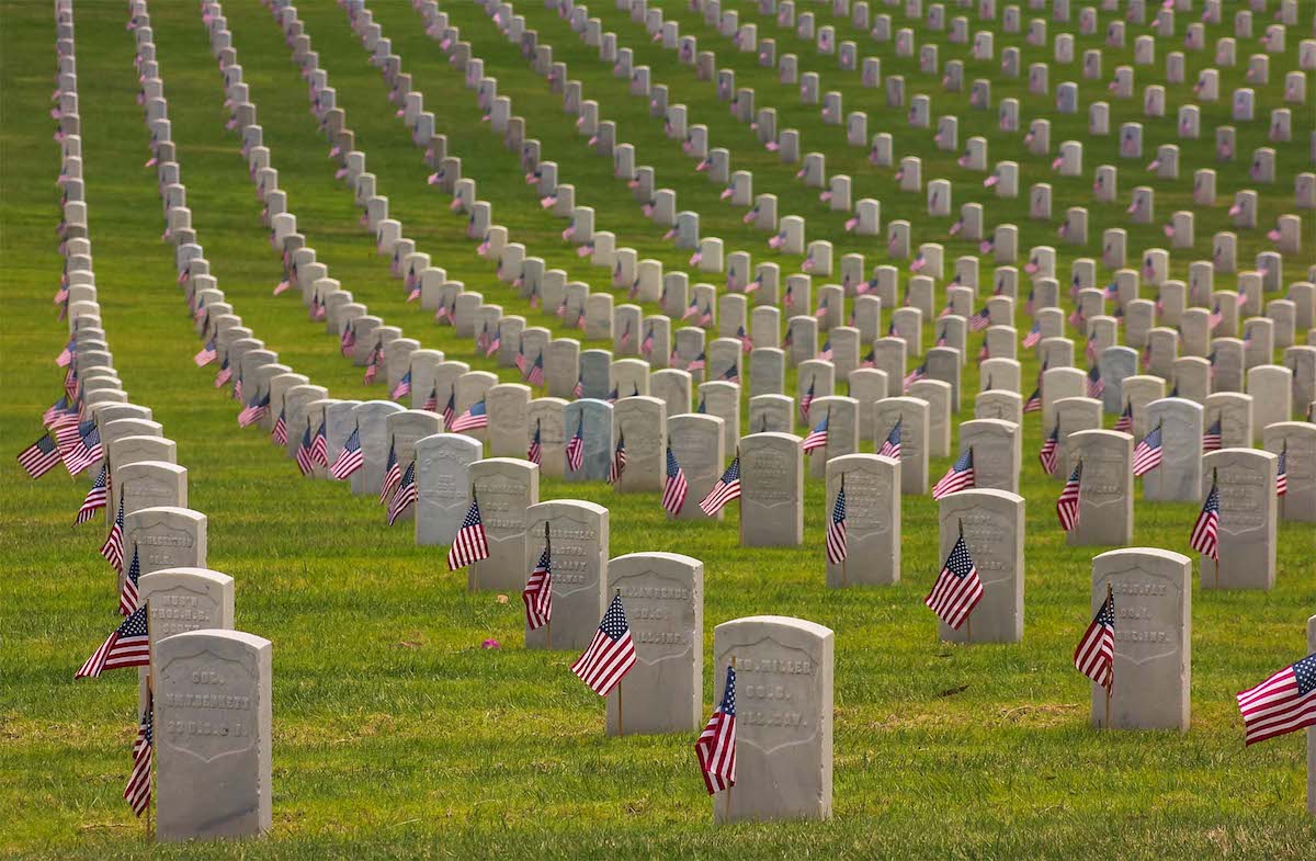 VA national memorial cemetery with rows of headstone of the same shape accompanied by small American flags