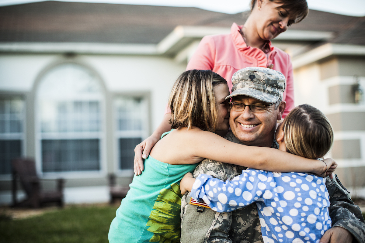 Army father hugs children son and daughter while mom stands behind.