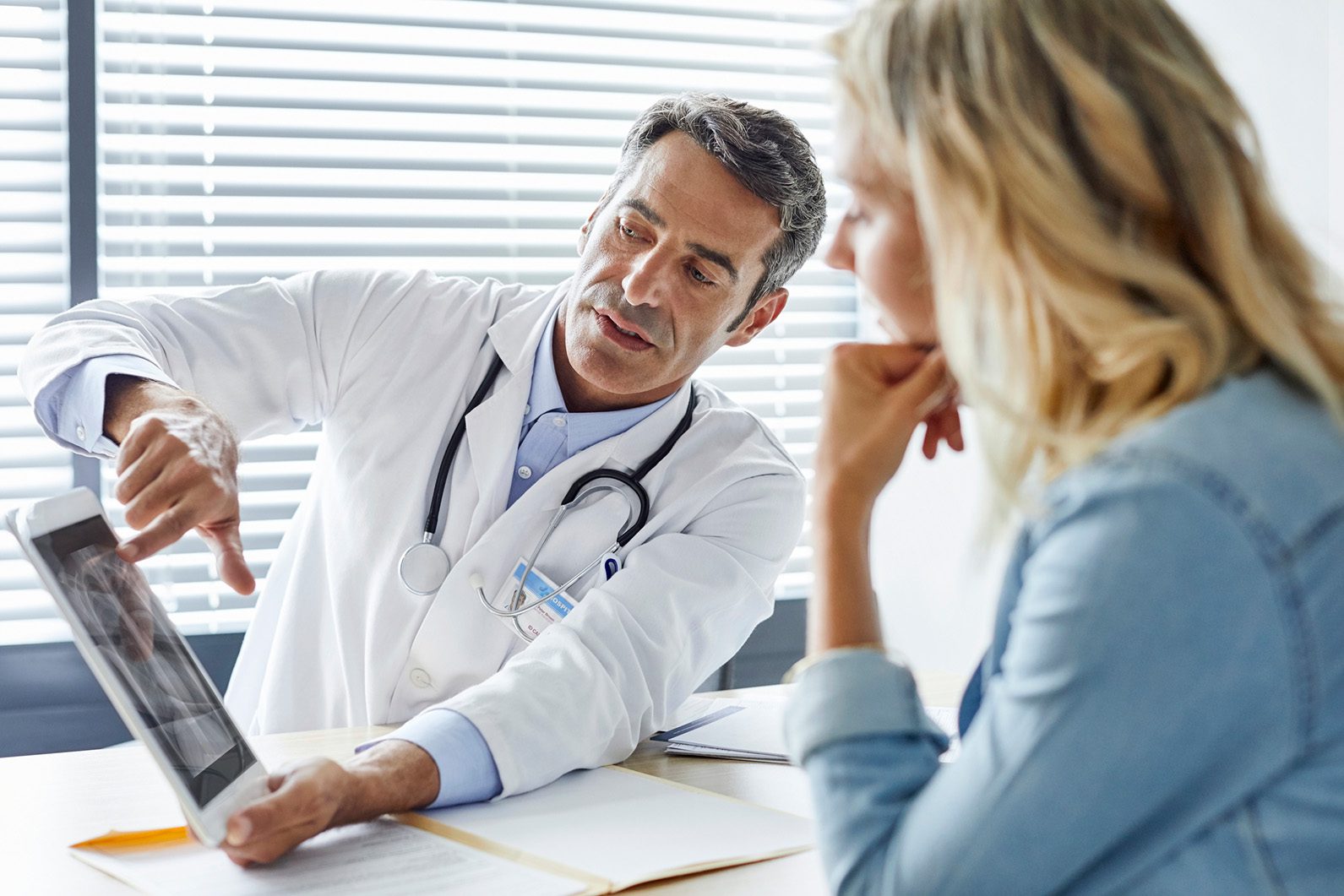 Male doctor in medical jacket talking with mature female patient about mesothelium looking at x-ray of chest