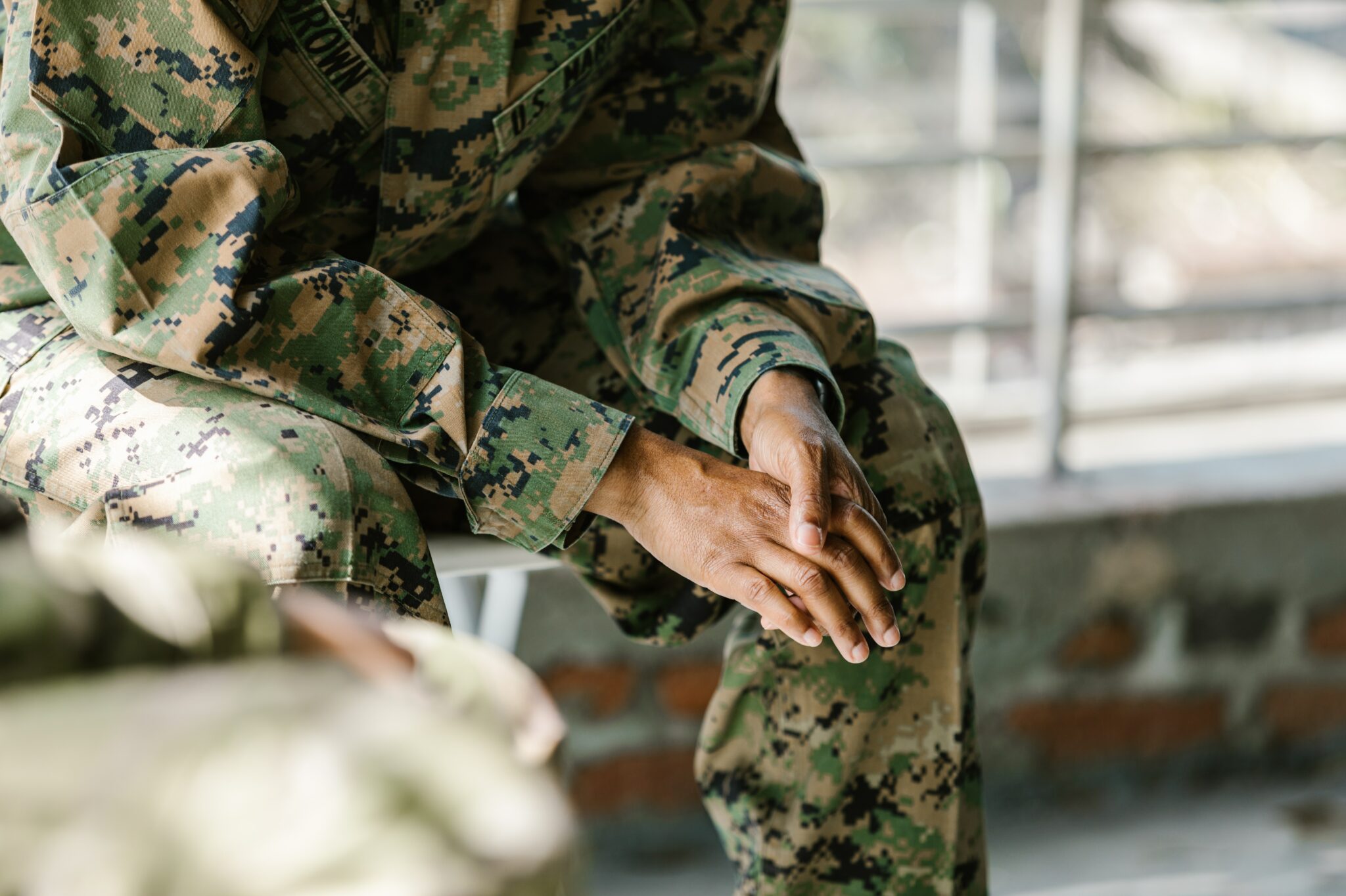 A man contemplating hiring a Camp Lejeune Attorney in brown and green military garb sitting and wringing his hands