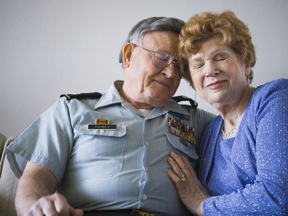 Older male veteran in uniform with mesothelioma embracing older female